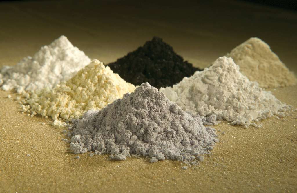 Six piles of rare earth oxide powders.